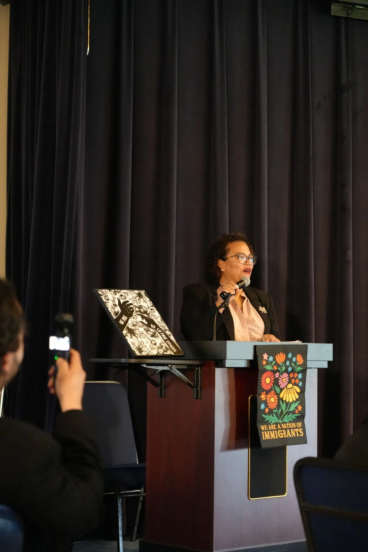 A symposium speaker speaks at a lectern in front of a dark curtain